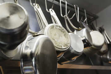 Close up of stainless steel pots and pans hanging on metal hooks on a shelf in a restaurant kitchen.