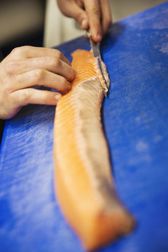 Close up of a chef cutting a fillet of salmon on a blue chopping board.