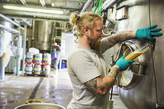 Man standing next to the door of a large stainless steel kettle in a brewery.
