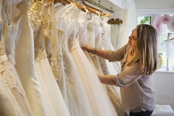 A sales assistant in a wedding dress shop, looking through the gowns hanging in the rails. 