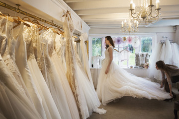 Rows of wedding dresses on display in a specialist wedding dress shop. A young woman trying on a wedding dress with a long train. 