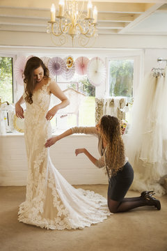 A dressmaker taking in a wedding dress, pinning and fitting it to the client, a young woman. A bride selecting her dress in a specialist shop. 
