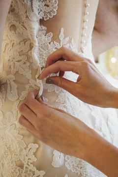 A dressmaker taking in a wedding dress, pinning and fitting it to the client. 