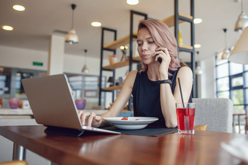 Business woman eats at a cafe and uses a smartphone and laptop.
