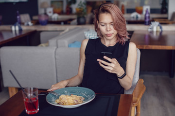 Attractive woman using smartphone and eating in a cafe.