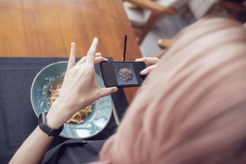 Attractive woman makes a photo of a carbonara paste in a cafe.