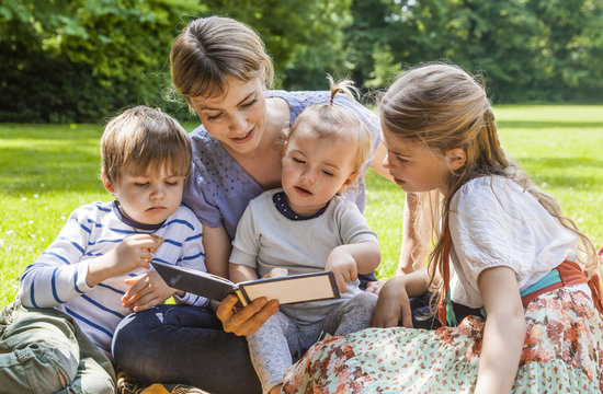Mother showing photo album to children on meadow