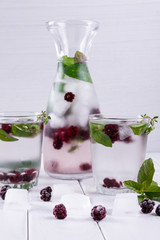 Mineral infused water with blackberry, ice, herb and mint leaves on white background, homemade detox soda water recipe.