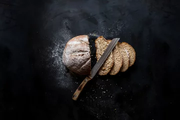 Zelfklevend Fotobehang Gesneden brood en een mes liggend op een zwart metalen tafel © Dima