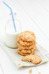 .A stack of cookies and a broken biscuits, milk bottle with a straw on a light wooden table on white background close up.