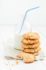 A stack of cookies and a bottle of milk with a straw on a light wooden table against a white background.