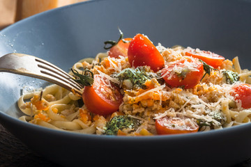 Pasta with tomato, parmesan and pesto closeup on a wooden table.