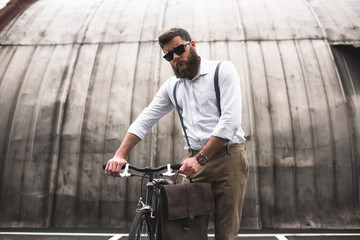 Fototapeta na wymiar successful fashionable bearded man in sunglasses standing with bicycle
