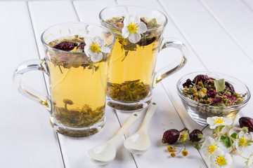Two cups of herbal tea with rosehip , chamomile, herbs on  white wooden table