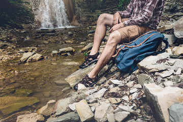 Unrecognizable Traveler With Backpack Sits On The River And Enjoys Surrounding View Exploring Adventure Hiking Concept