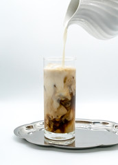 pouring milk into a glass of coffee