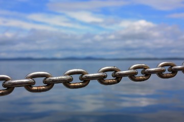 Metal chain on a sailboat with blue sky and water in background.