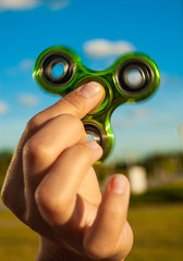 Hand holding popular green fidget spinner toy on sky background