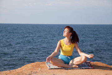 Fototapeta na wymiar the girl is engaged in yoga sits on the cliff by the sea