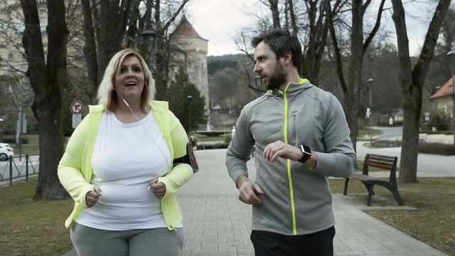 Fitness trainer in town park running with overweight woman.