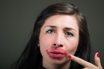 Obraz premium Beautiful natural girl woman pointing with her hand to her face a lips pink mask, spa treatments. Cosmetology in a dark background