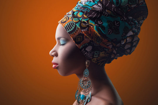 young beautiful fashion model with traditional african style with scarf, earrings and makeup on orange background.