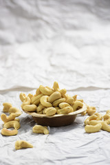 There is brown wooden bowl filled with cashew in and some fallen out of it and it isshot on white background.