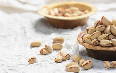 There are two brown bowl filled with pistachio filled in it. one bowl is in the front and in the background another bowl of pistchio is placed and it is shot on white background.