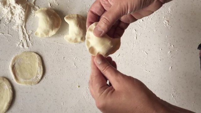 Woman mold ukrainian national vareniks with potato. Table with flour. And ready vareniks on the wooden board. Home cooking process of a tasty dumplings. Pierogies
