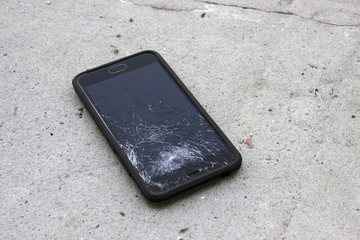 The phone with the broken screen lies on the asphalt