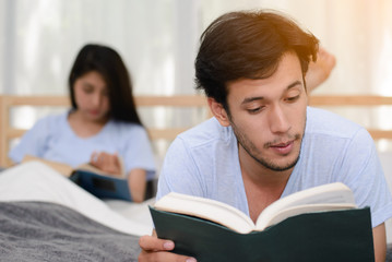 Couple reading a book together in bedroom, focused on male.