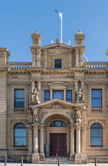 Hobart, Australia - March 19. 2017: Tasmania. Beige stone Old Custom House converted into Tasman Museum and Art Gallery. Center of facade with monumental entrance. Flag on top with blue sky.