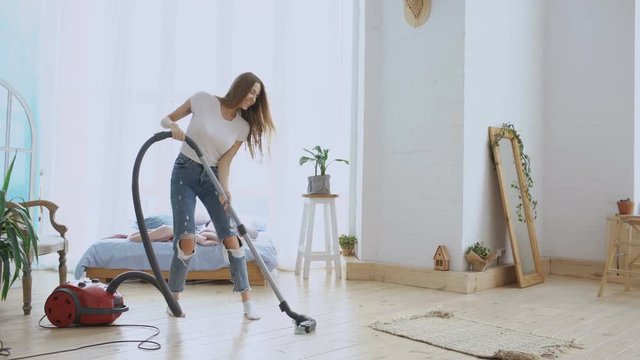 Young woman having fun cleaning house with vacuum cleaner dancing and singing at home