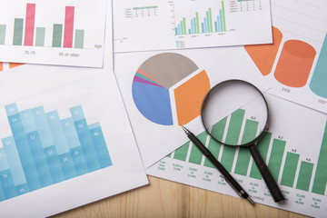 Magnifying glass and documents with analytics data lying on wood table