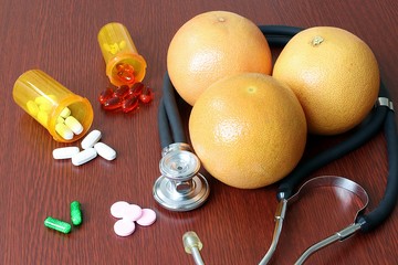 Spilled prescription pills next to grapefruits and stethoscope