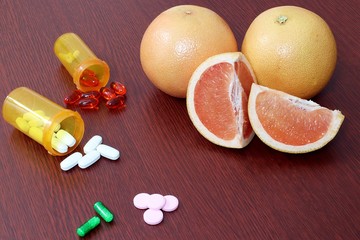 whole and sliced juicy grapefruit next to medication tablets