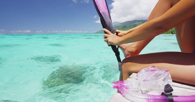 Snorkel girl putting on snorkeling fins getting ready for swim in summer ocean turquoise waters. Sports activity leisure fun sport travel lifestyle woman going swimming wearing pink watersport gear.