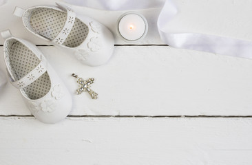 Christening background with white baby booties, crystal cross and satin ribbon isolated on white plank floor