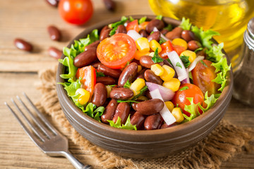 Fresh vegetable salad with beans in ceramic bowl on wooden table.