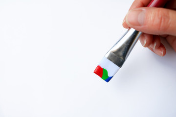 Hand holding a paintbrush with colors of red, blue and green