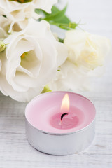 Arrangement of white eustoma flowers and pink lit candle