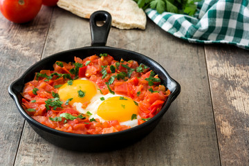 Shakshuka in iron frying pan on wooden table. Typical food in Israel.
