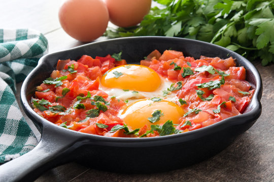 Shakshuka in iron frying pan on wooden table. Typical food in Israel.
