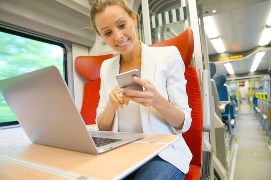 Businesswoman in train working on laptop and talking on phone