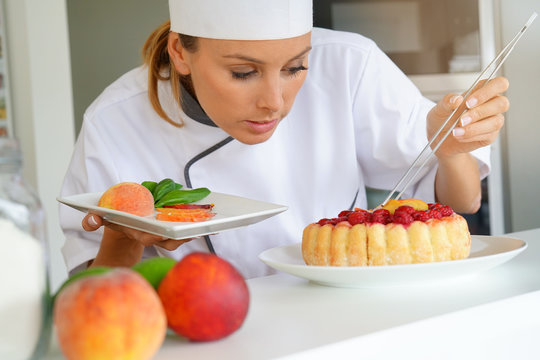 Pastry chef in professional kitchen decorating raspberry cake with fruits