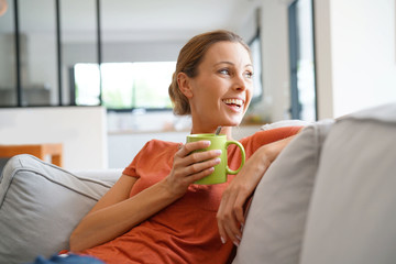 Cheerful woman relaxing in sofa and drinking tea