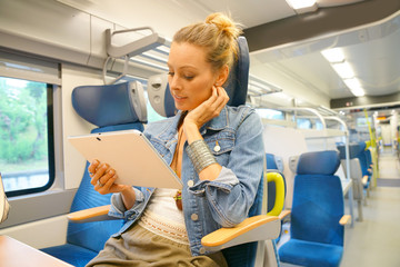 Smiling young woman in train connected on tablet