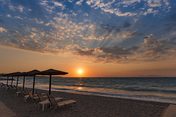 Beautiful sunset contre-jour on the sea shore, in a beach resort, with comfortable sunbeds and umbrellas