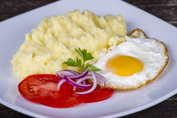 Mashed potatoes with fried eggs and tomato.