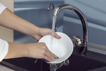 Woman hands rinsing dishes under running water in the sink.